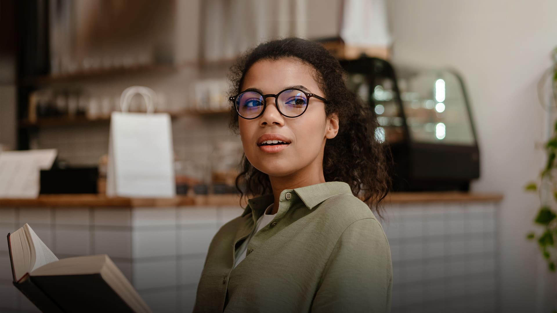 Woman wearing dark-framed eyeglasses while holding an open book